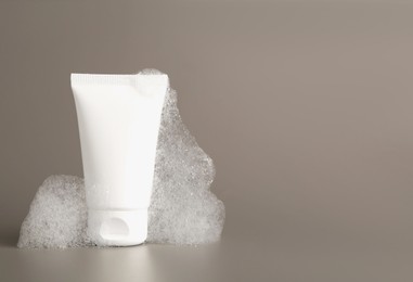 Tube of cosmetic product with foam on grey background, space for text