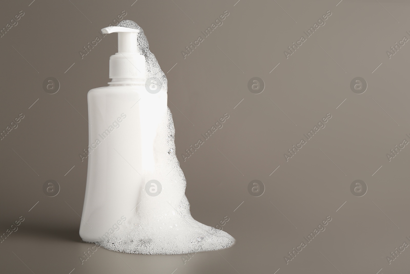 Photo of Bottle of cosmetic product with foam on grey background, space for text