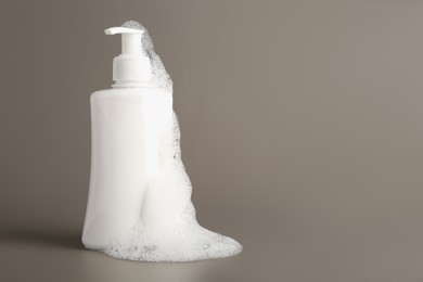 Bottle of cosmetic product with foam on grey background, space for text