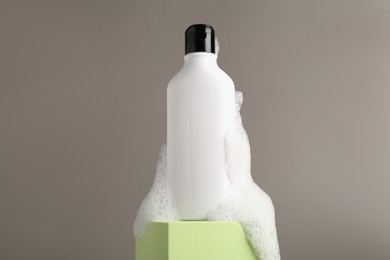 Bottle of cosmetic product with foam on podium against grey background