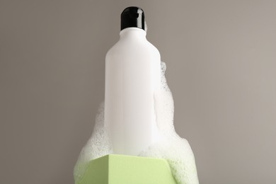 Photo of Bottle of cosmetic product with foam on podium against grey background