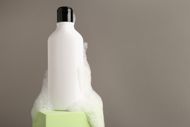 Bottle of cosmetic product with foam on podium against grey background, space for text