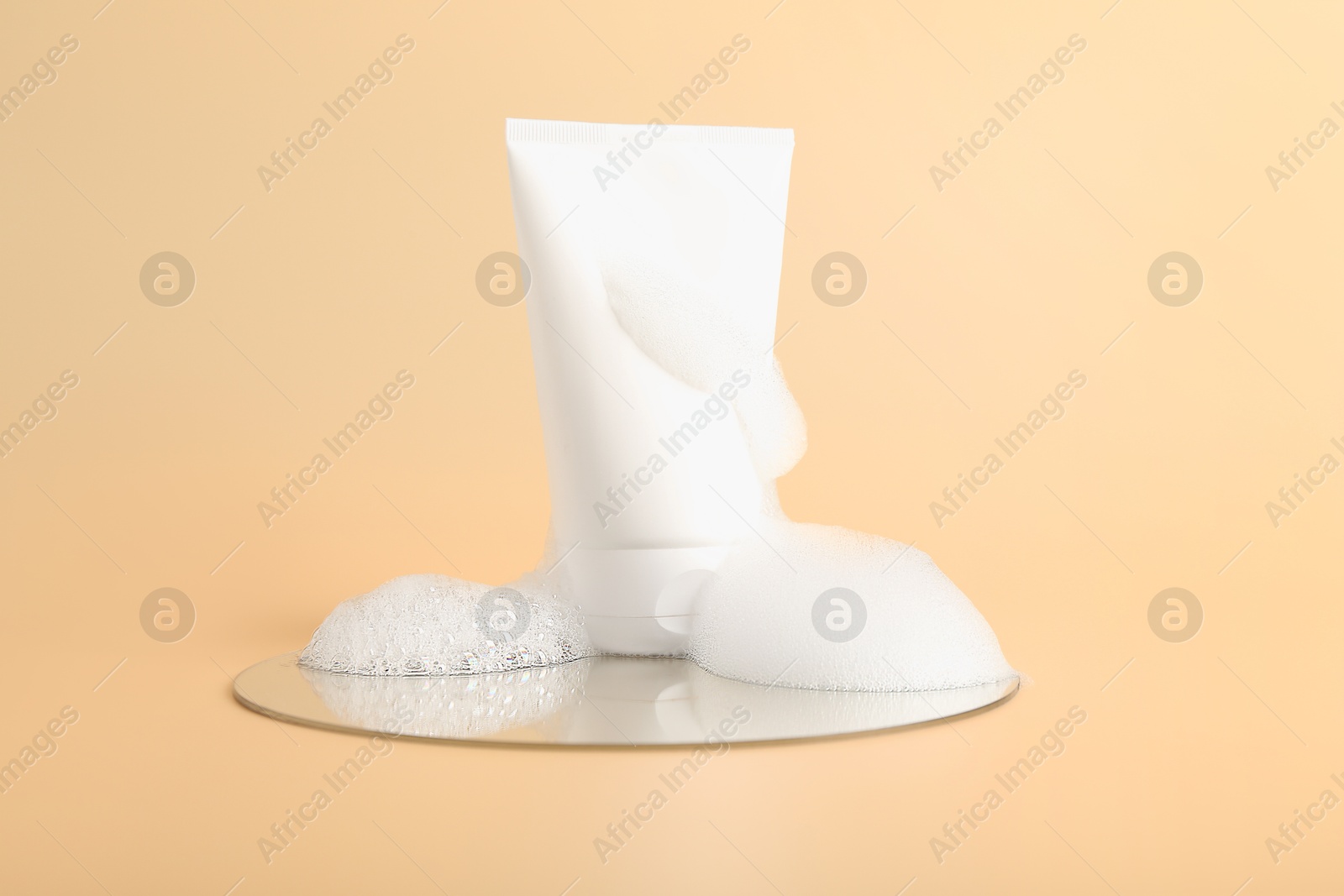 Photo of Tube of cosmetic product with foam and mirror on beige background