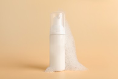 Bottle of cosmetic product with foam on beige background