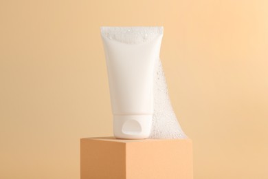 Photo of Tube of cosmetic product with foam on podium against beige background