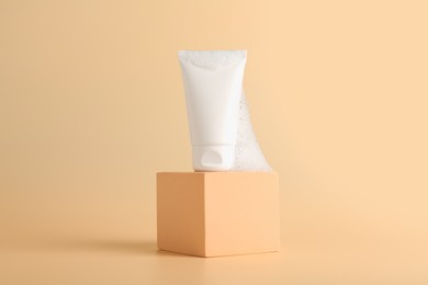 Photo of Tube of cosmetic product with foam on podium against beige background