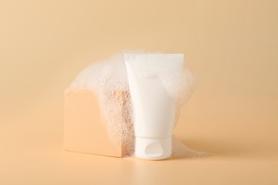 Photo of Tube of cosmetic product with foam and podium on beige background