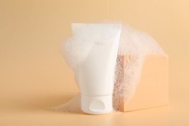 Tube of cosmetic product with foam and podium on beige background