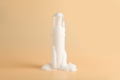 Photo of Bottle of cosmetic product with foam on beige background