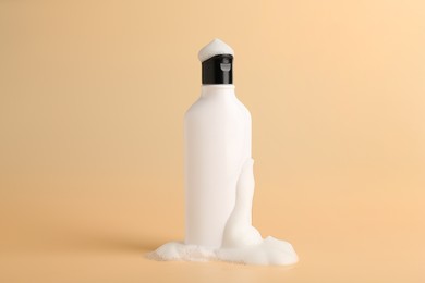 Bottle of cosmetic product with foam on beige background