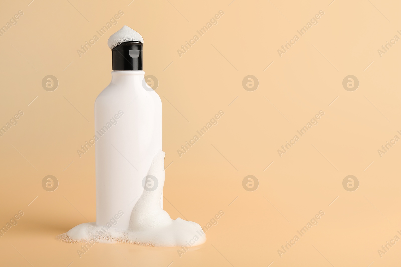 Photo of Bottle of cosmetic product with foam on beige background, space for text