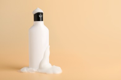 Photo of Bottle of cosmetic product with foam on beige background, space for text