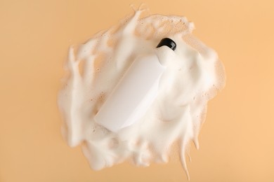 Photo of Bottle of cosmetic product with foam on beige background, top view