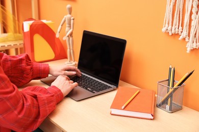 Photo of Woman working on laptop at wooden desk indoors, closeup