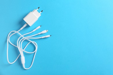 Photo of USB power adapter with triple charge cable on light blue background, top view. Space for text