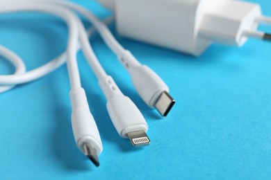 Photo of Triple charge cable and USB power adapter on light blue background, closeup. Space for text