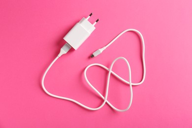 Photo of USB power adapter with charge cable on pink background, top view