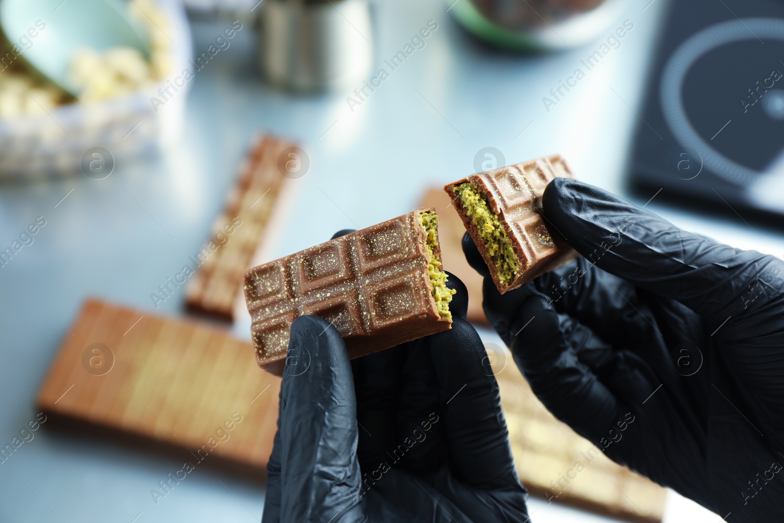 Photo of Woman holding pieces of tasty Dubai chocolate with pistachios and knafeh at grey table, closeup