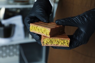 Woman holding pieces of tasty Dubai chocolate with pistachios and knafeh indoors, closeup. Space for text