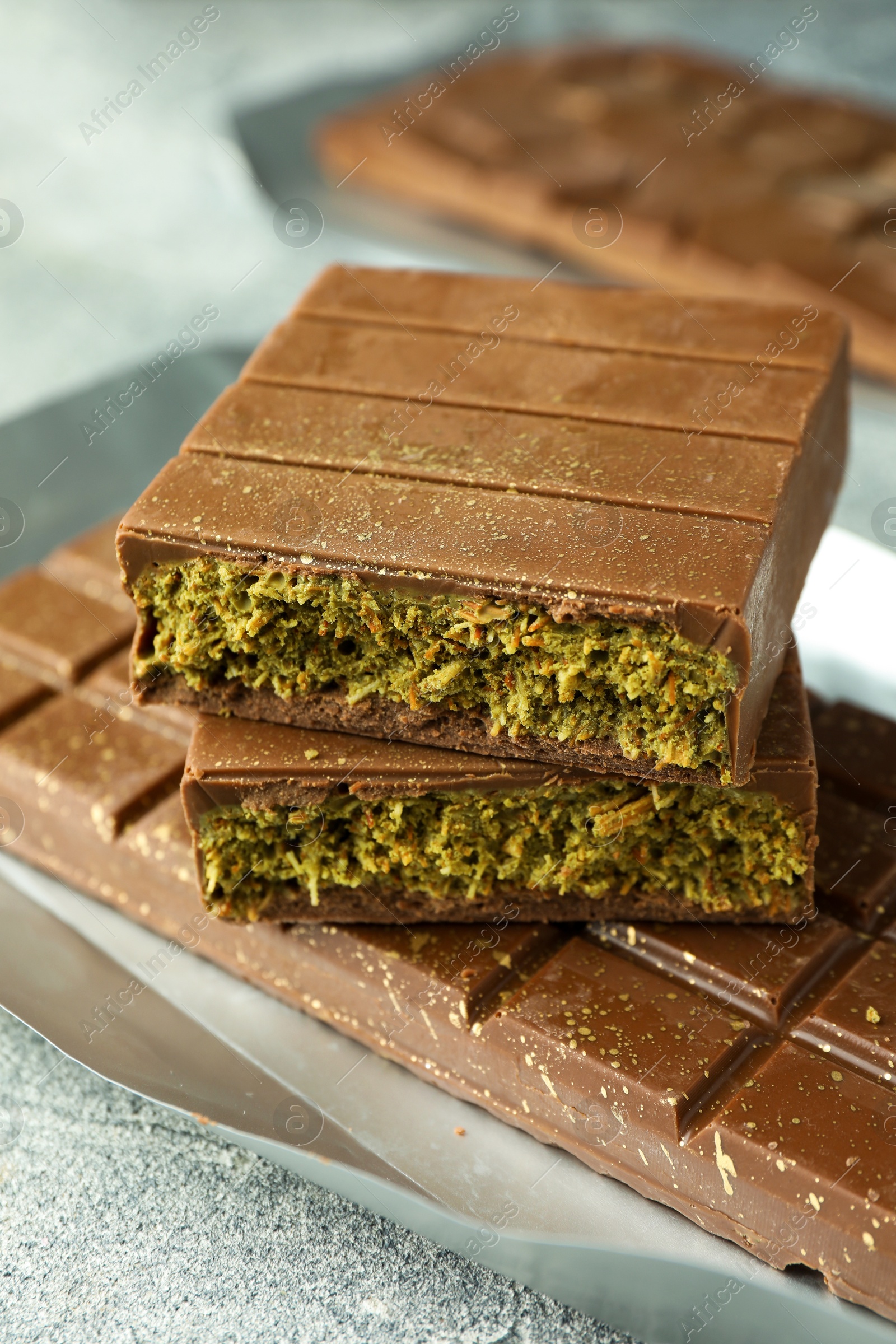 Photo of Tasty Dubai chocolate with pistachios and knafeh on grey textured table, closeup