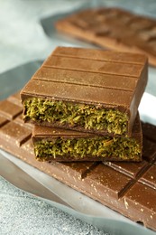 Photo of Tasty Dubai chocolate with pistachios and knafeh on grey textured table, closeup