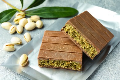 Photo of Pieces of tasty Dubai chocolate with pistachios and knafeh on grey textured table, closeup