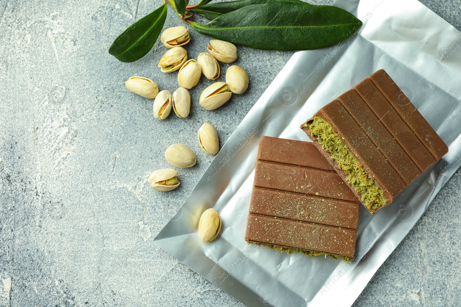 Photo of Pieces of tasty Dubai chocolate with pistachios and knafeh on grey textured table, flat lay. Space for text