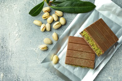 Pieces of tasty Dubai chocolate with pistachios and knafeh on grey textured table, flat lay. Space for text