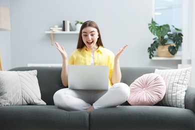 Emotional young woman with laptop on sofa at home