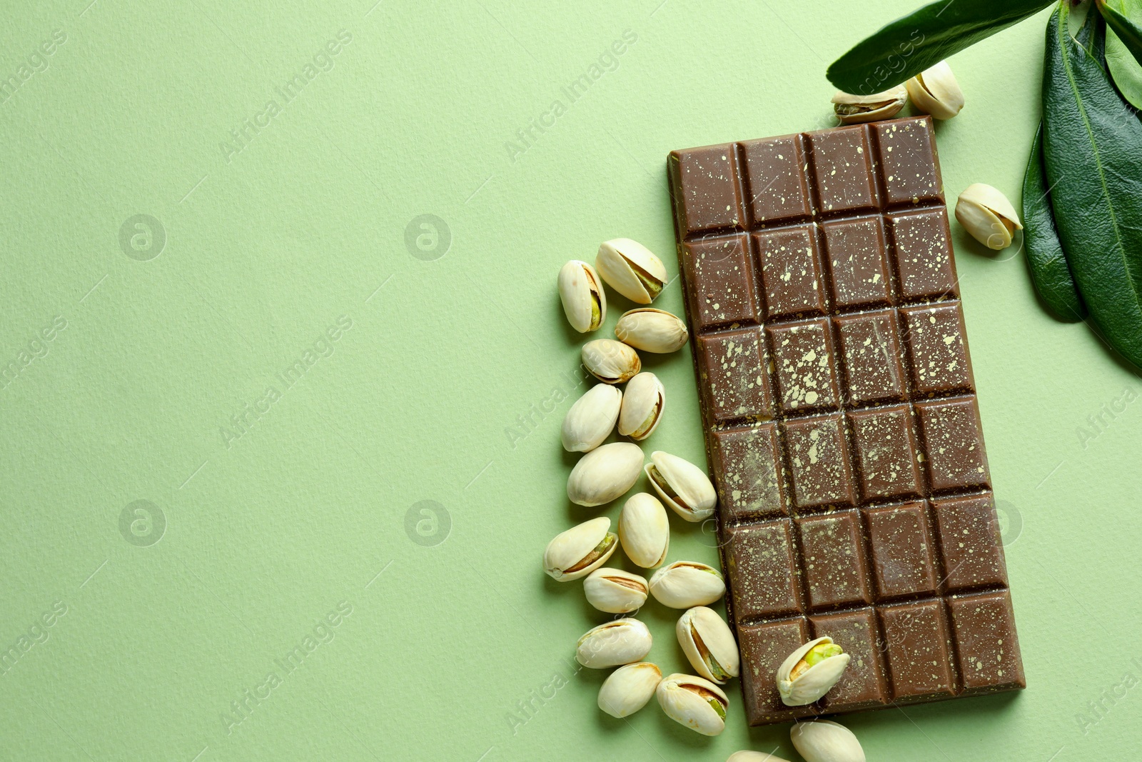 Photo of Delicious Dubai chocolate with pistachios and knafeh on green background, flat lay. Space for text