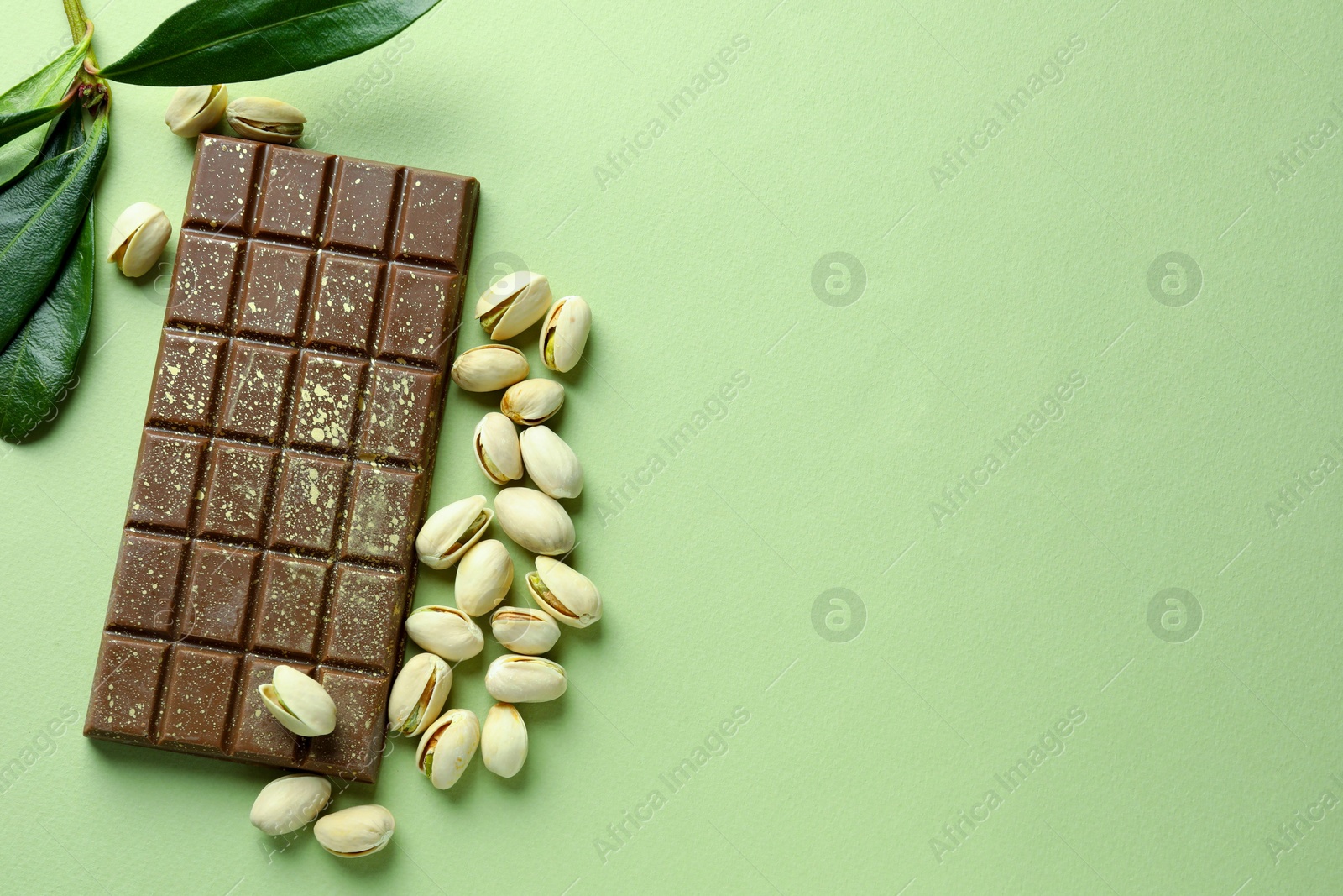 Photo of Delicious Dubai chocolate with pistachios and knafeh on green background, flat lay. Space for text