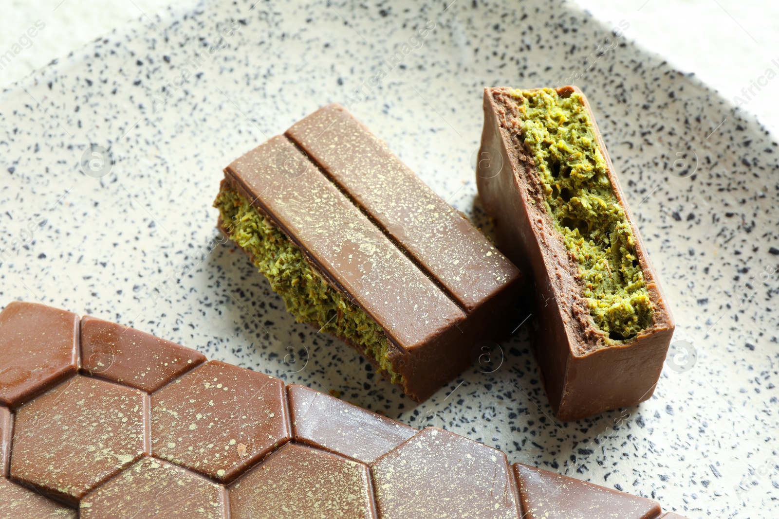 Photo of Pieces of delicious Dubai chocolate with pistachios and knafeh on plate, closeup