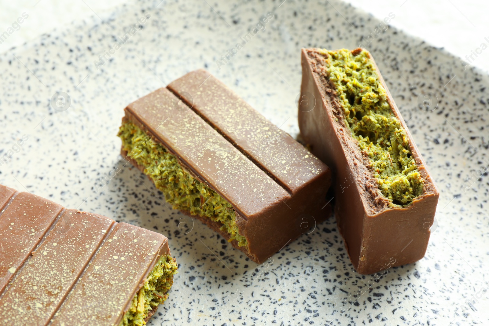 Photo of Pieces of delicious Dubai chocolate with pistachios and knafeh on plate, closeup