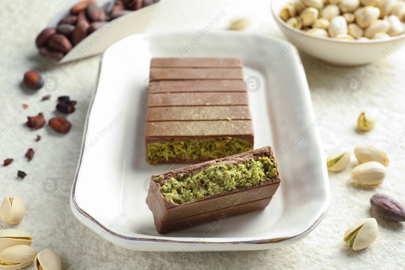 Photo of Pieces of delicious Dubai chocolate with pistachios, knafeh and cocoa beans on light textured table, closeup