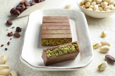 Pieces of delicious Dubai chocolate with pistachios, knafeh and cocoa beans on light textured table, closeup