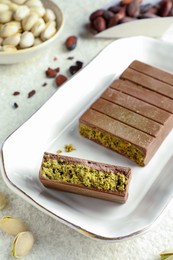 Pieces of delicious Dubai chocolate with pistachios, knafeh and cocoa beans on light textured table, closeup