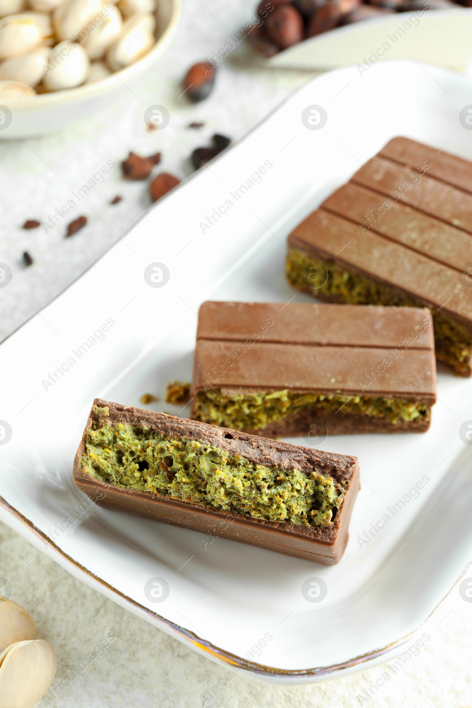 Photo of Pieces of delicious Dubai chocolate with pistachios and knafeh on light textured table, closeup