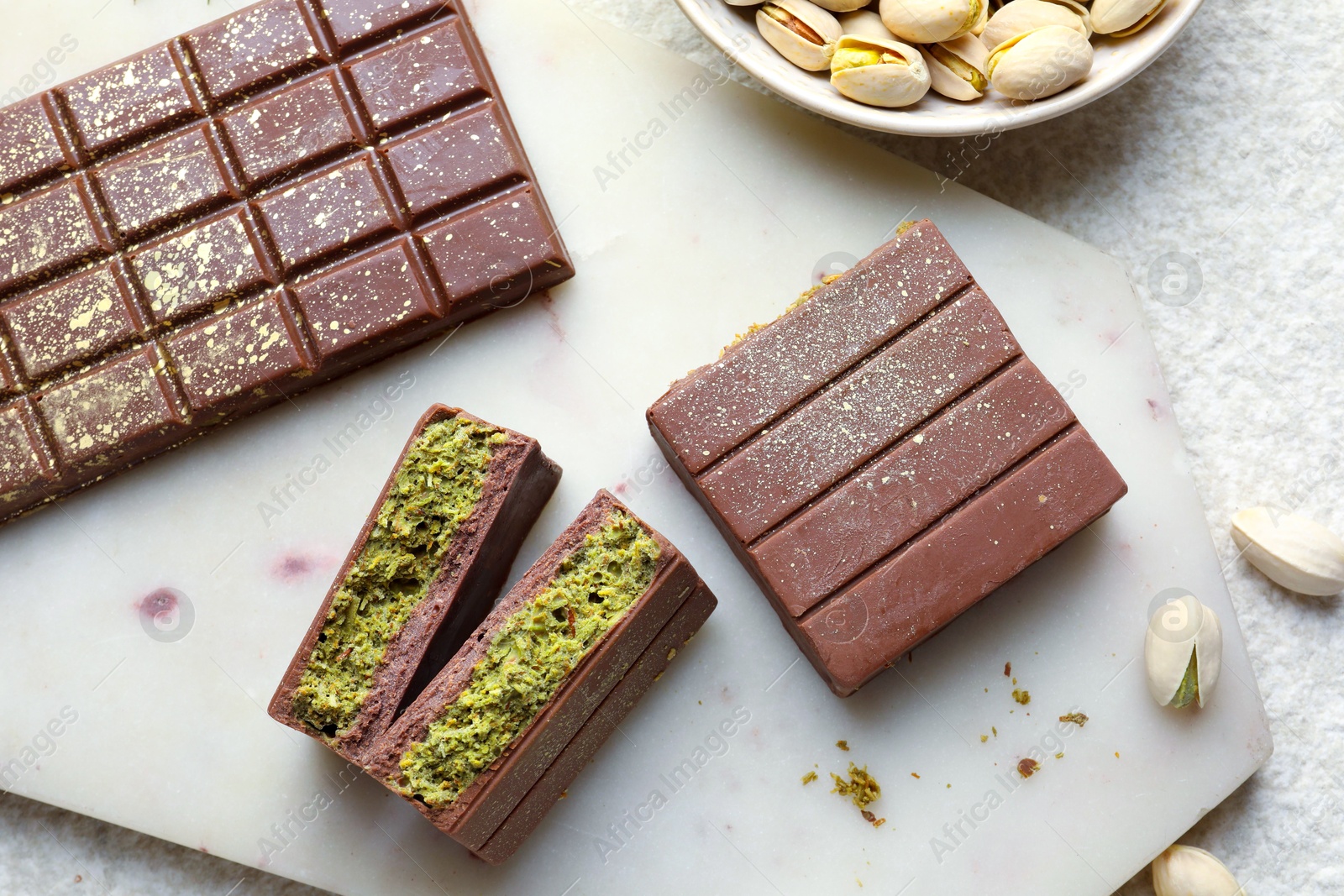 Photo of Delicious Dubai chocolate with pistachios and knafeh on light textured table, flat lay