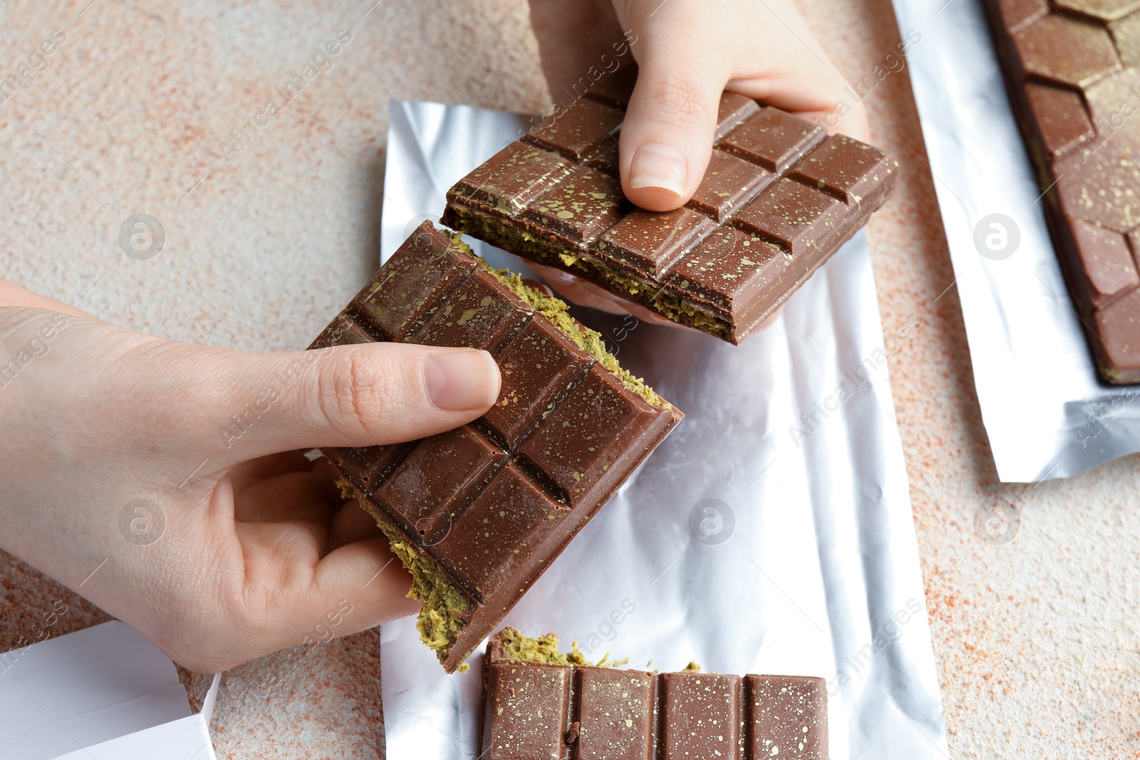 Photo of Woman breaking delicious Dubai chocolate bar with pistachios and knafeh at color textured table, above view