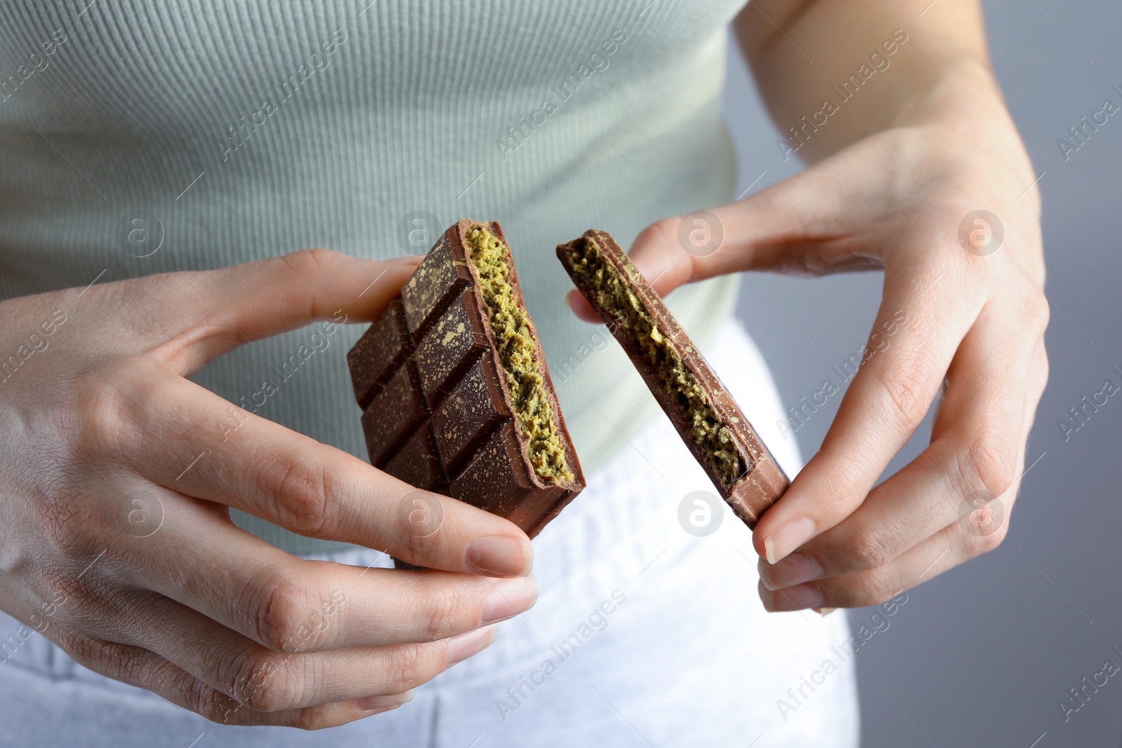 Photo of Woman holding pieces of delicious Dubai chocolate with pistachios and knafeh on grey background, closeup