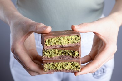 Photo of Woman holding pieces of delicious Dubai chocolate with pistachios and knafeh on grey background, closeup