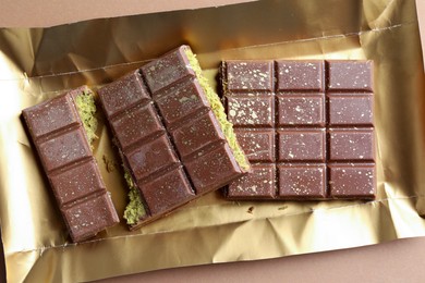 Photo of Pieces of delicious Dubai chocolate with pistachios and knafeh on dark beige background, top view