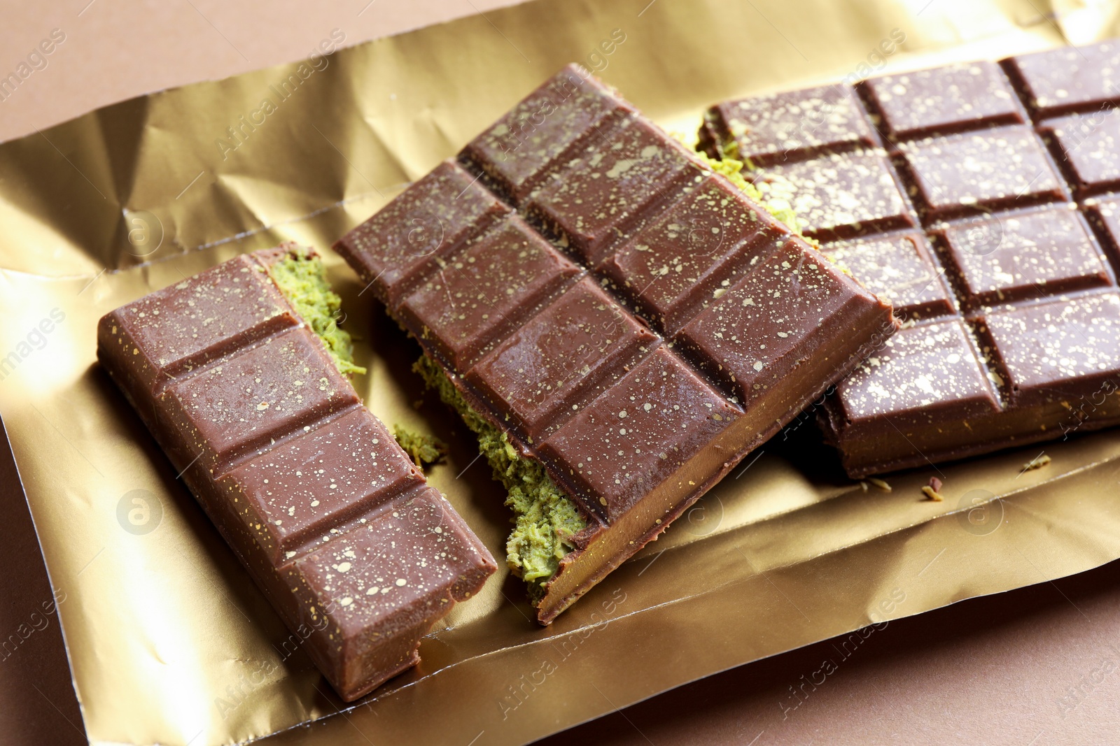 Photo of Pieces of delicious Dubai chocolate with pistachios and knafeh on dark beige background, closeup