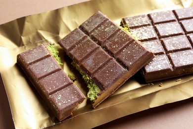 Photo of Pieces of delicious Dubai chocolate with pistachios and knafeh on dark beige background, closeup