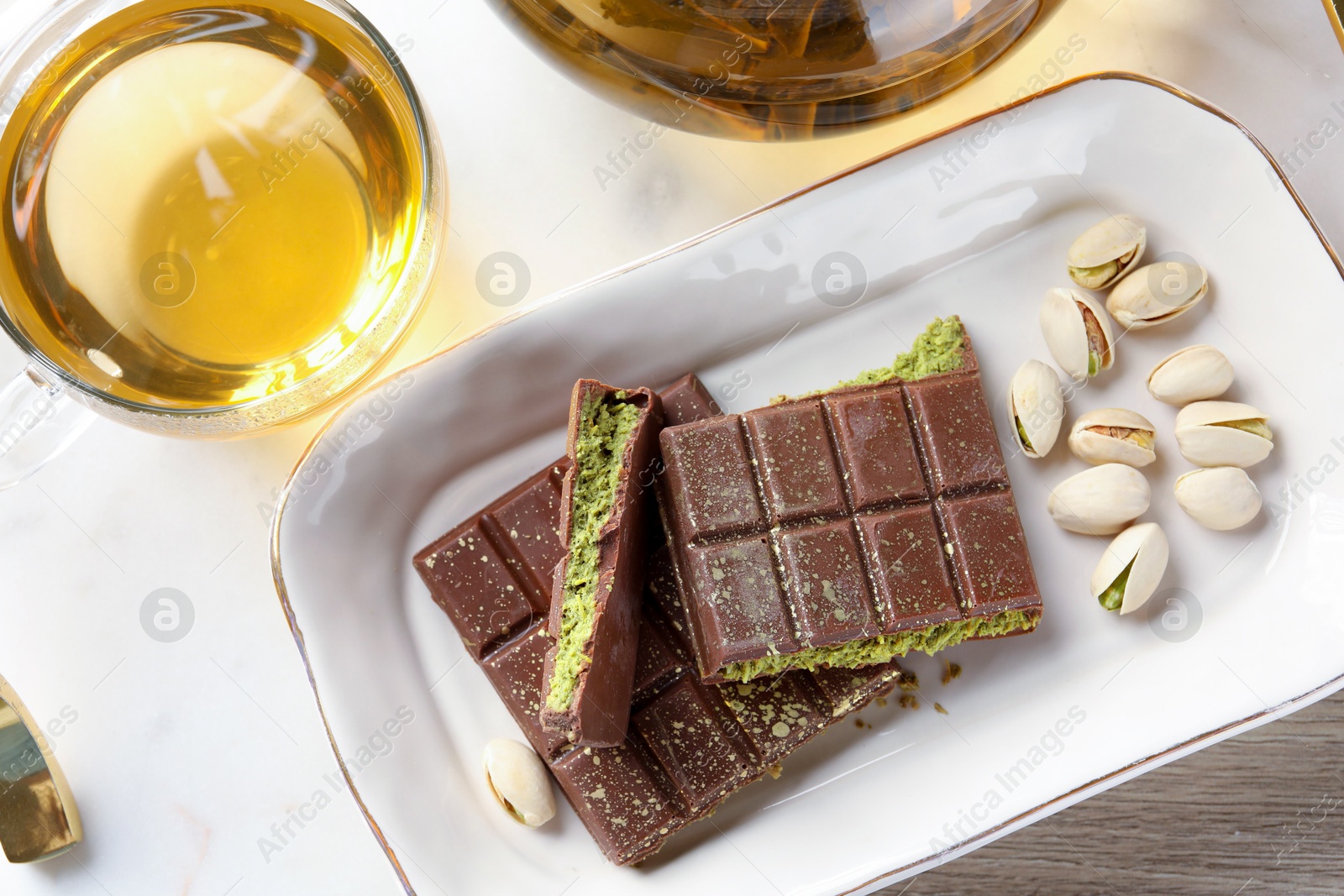 Pieces of delicious Dubai chocolate with pistachios, knafeh and tea on wooden table, flat lay Photo of Pieces of delicious Dubai chocolate with pistachios, knafeh and tea on wooden table, flat lay