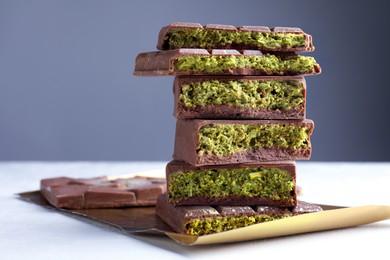 Photo of Pieces of delicious Dubai chocolate with pistachios and knafeh on white table, closeup. Space for text