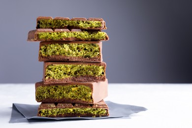 Photo of Pieces of delicious Dubai chocolate with pistachios and knafeh on white table, closeup. Space for text