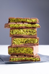 Photo of Pieces of delicious Dubai chocolate with pistachios and knafeh on white table, closeup