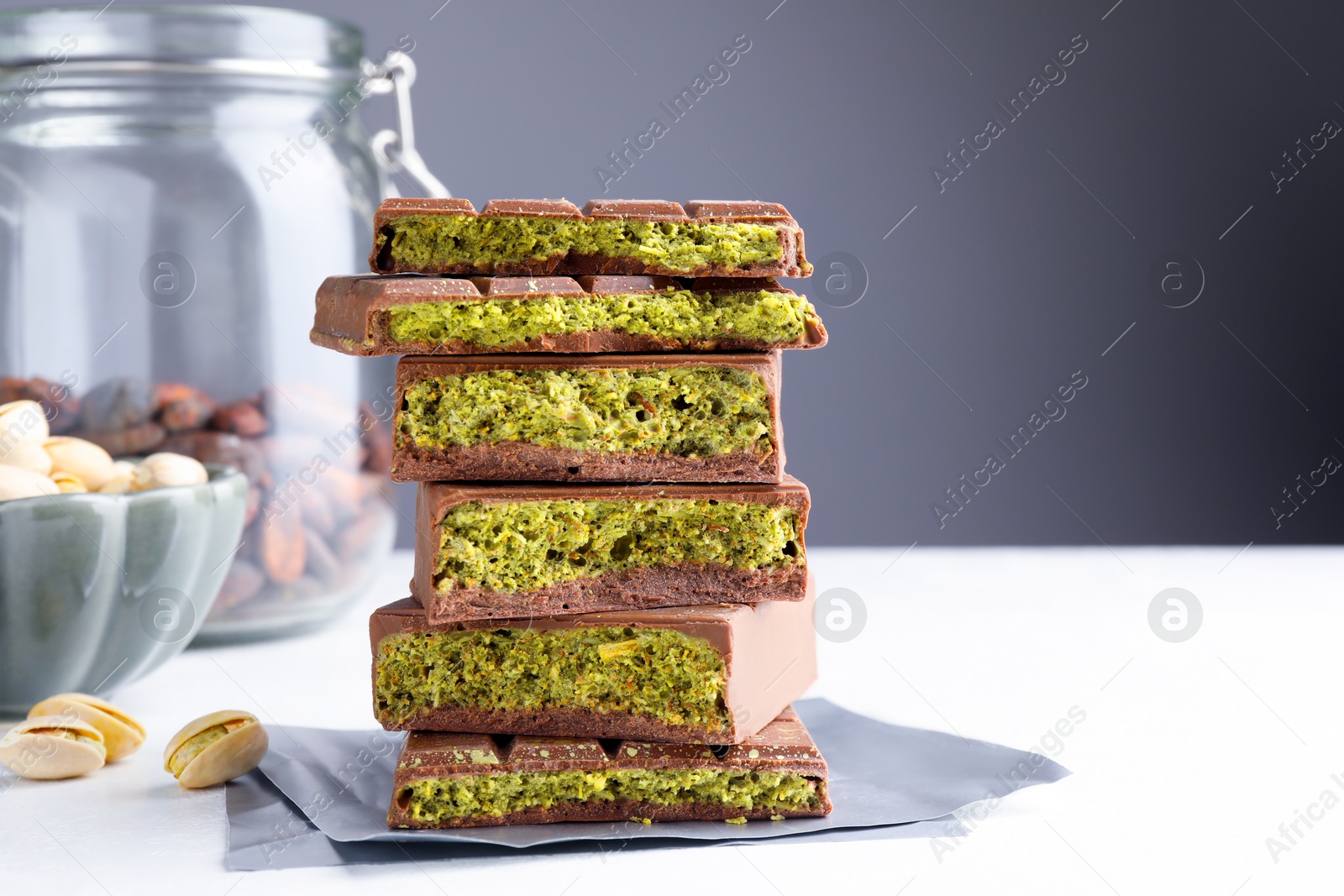 Pieces of delicious Dubai chocolate with pistachios, knafeh and cocoa beans on white table, closeup. Space for text Photo of Pieces of delicious Dubai chocolate with pistachios, knafeh and cocoa beans on white table, closeup. Space for text