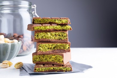 Photo of Pieces of delicious Dubai chocolate with pistachios, knafeh and cocoa beans on white table, closeup. Space for text